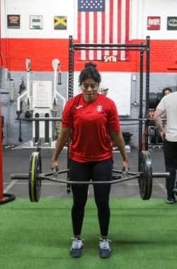 Female athlete at lifting a loaded barbell during a cross-training class, focusing on strength.