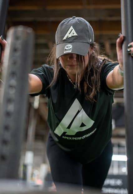 Focused female athlete wearing APEX gear completing a sled push exercise at Apex Performance Gym.