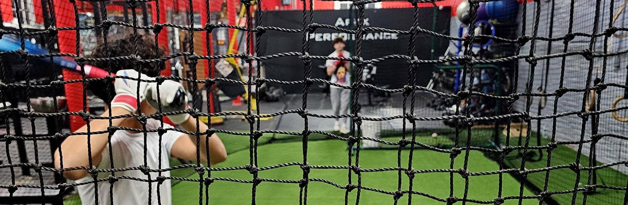 Behind-the-net perspective of a baseball athlete mid-swing at Apex Performance Gym