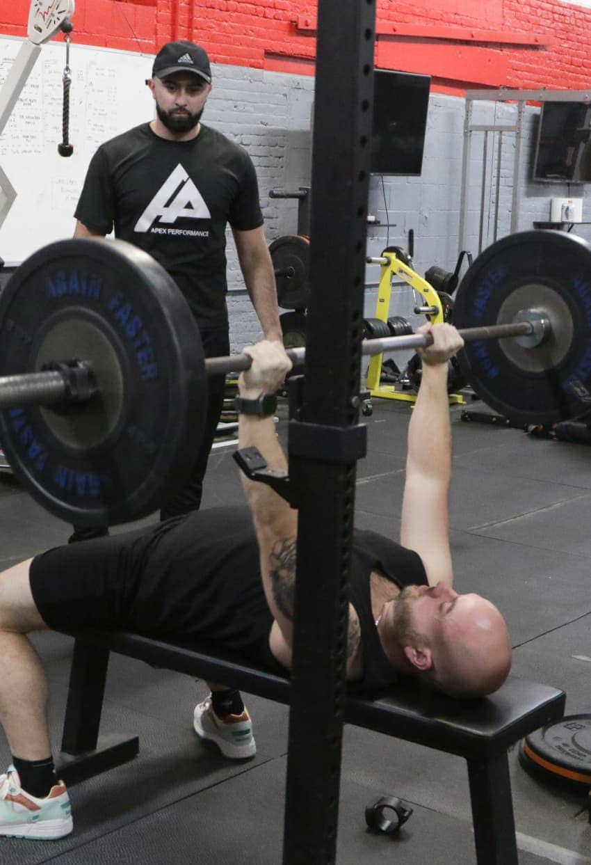 Personal trainer supervising a bench press session at Apex Performance Gym, highlighting hands-on coaching.